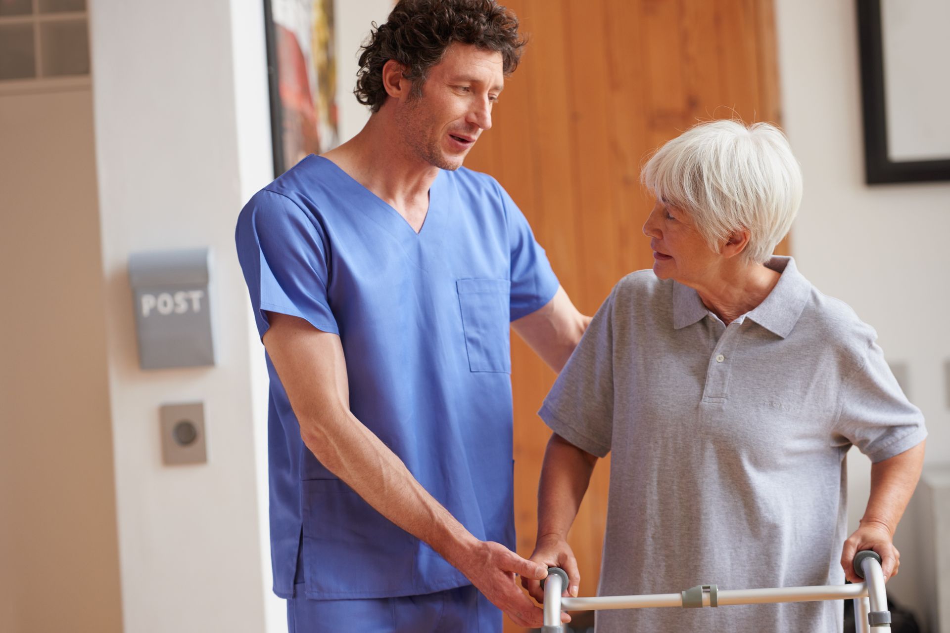 Therapeut begleitet eine Seniorin beim Gehtraining mit Rollator