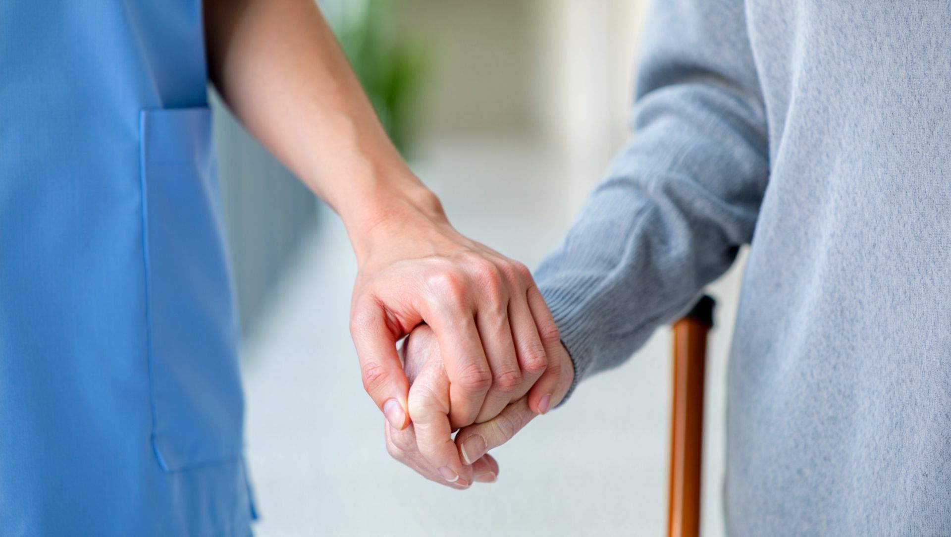 Pflegehand hält stützend die Hand eines Seniors mit Gehstock